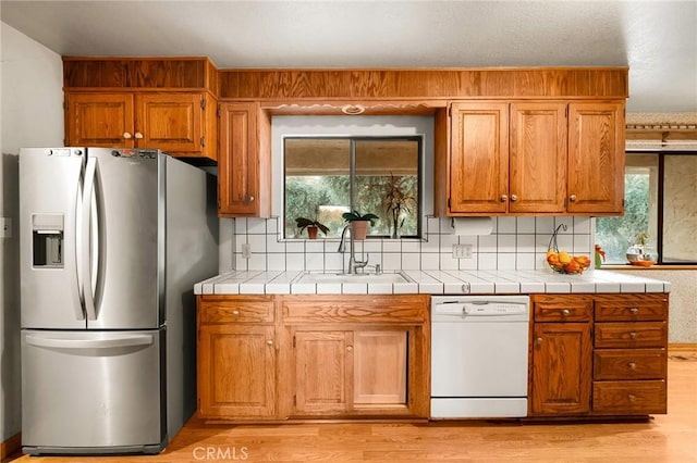 kitchen featuring sink, tile countertops, dishwasher, and stainless steel refrigerator with ice dispenser