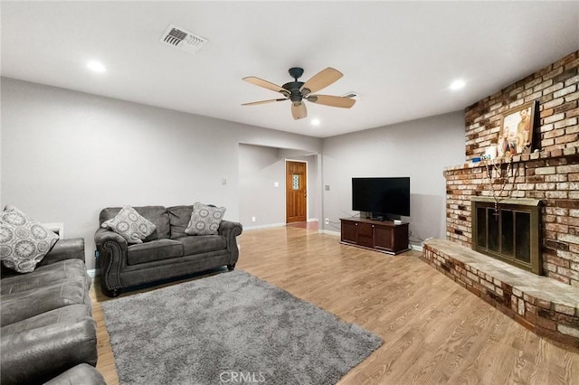 living room featuring a brick fireplace, ceiling fan, and light wood-type flooring