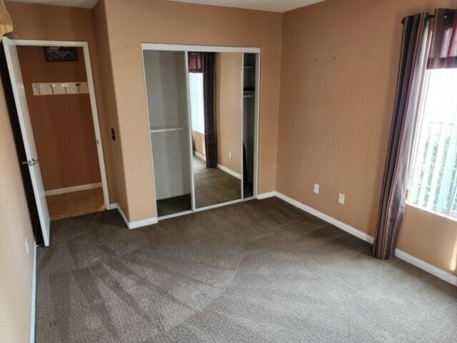 unfurnished bedroom with multiple windows, dark carpet, and a closet