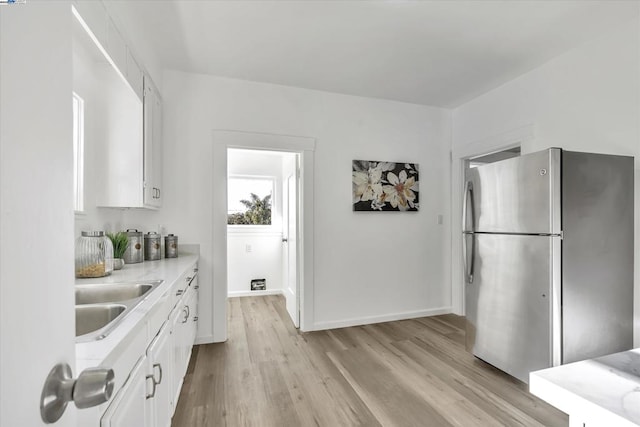 kitchen with white cabinetry, stainless steel fridge, light hardwood / wood-style floors, and sink