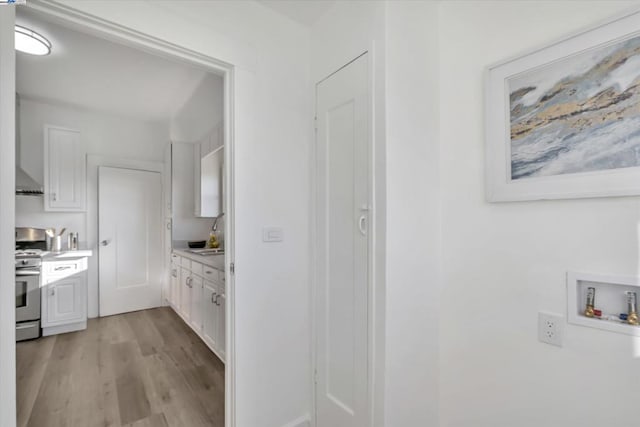 interior space with white cabinetry, sink, stainless steel stove, and light hardwood / wood-style flooring