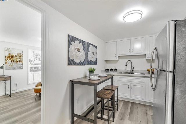 kitchen featuring white cabinetry, sink, stainless steel refrigerator, and light hardwood / wood-style flooring