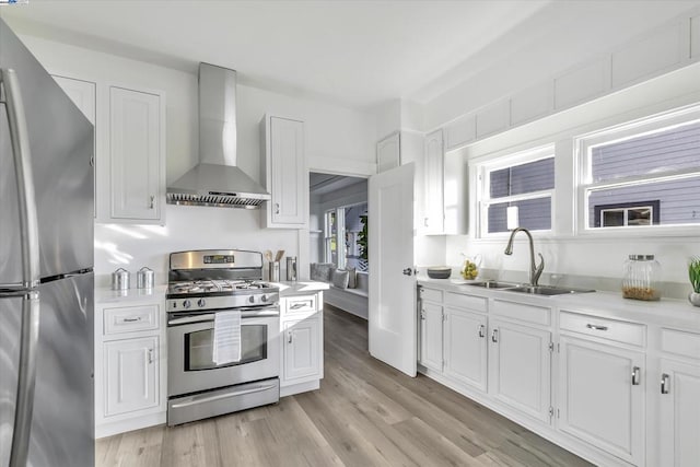 kitchen featuring sink, white cabinetry, stainless steel appliances, light hardwood / wood-style floors, and wall chimney range hood