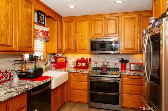 kitchen with stainless steel appliances, sink, backsplash, and light stone counters