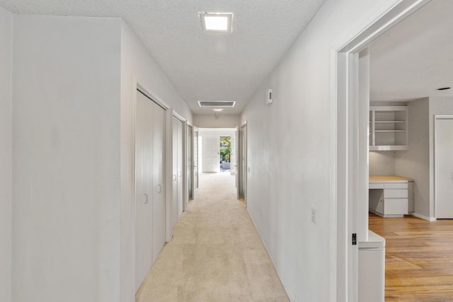 corridor featuring light carpet and a textured ceiling