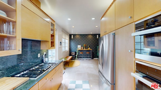 kitchen with stainless steel appliances, tasteful backsplash, light brown cabinetry, and dark stone counters