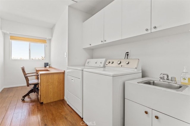 clothes washing area with cabinets, washing machine and dryer, sink, and light hardwood / wood-style flooring