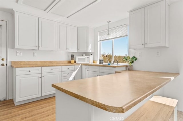 kitchen with white cabinetry, decorative light fixtures, kitchen peninsula, and sink