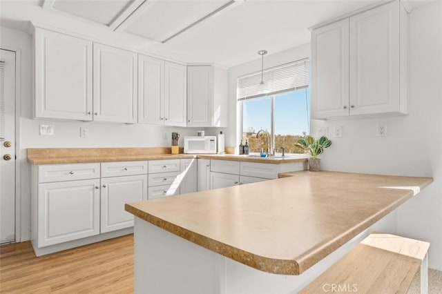 kitchen featuring white microwave, white cabinets, a peninsula, and a sink