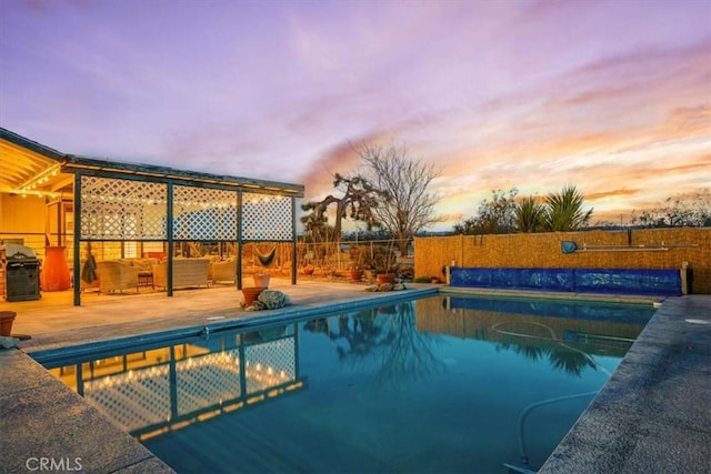 pool at dusk with area for grilling and a patio