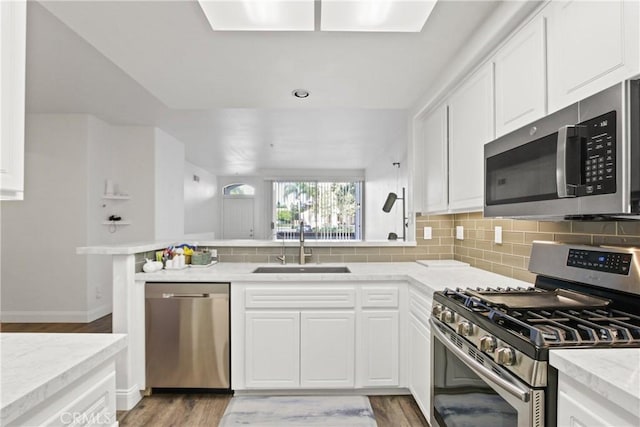 kitchen featuring sink, light hardwood / wood-style flooring, stainless steel appliances, white cabinets, and kitchen peninsula