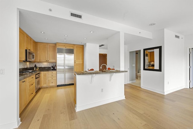 kitchen featuring tasteful backsplash, visible vents, a breakfast bar, stainless steel appliances, and light wood-type flooring