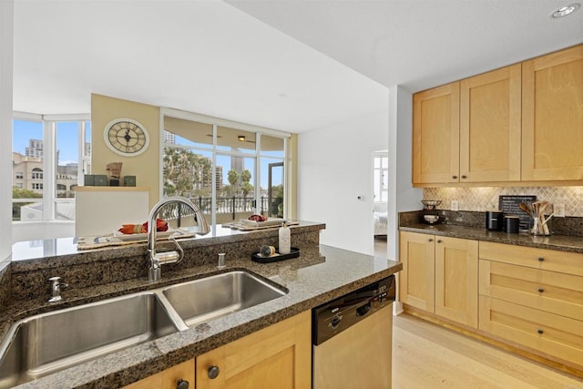 kitchen featuring dark stone counters, decorative backsplash, light brown cabinetry, stainless steel dishwasher, and a sink