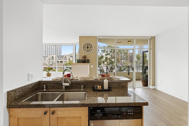 kitchen with dark stone counters, a sink, dishwasher, light brown cabinetry, and light wood finished floors