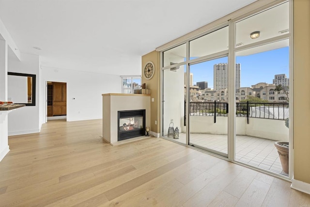 unfurnished living room with a view of city, light wood-type flooring, a multi sided fireplace, and baseboards