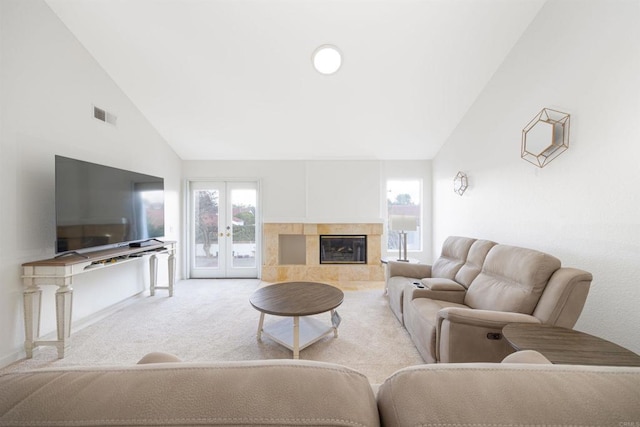 living room featuring a tiled fireplace, light colored carpet, high vaulted ceiling, and french doors