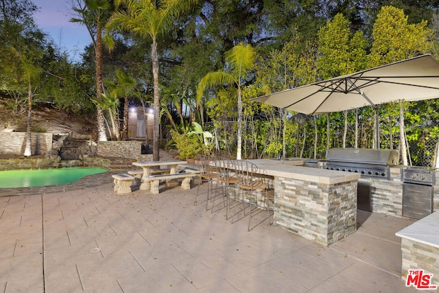 patio terrace at dusk featuring a bar, a grill, and an outdoor kitchen