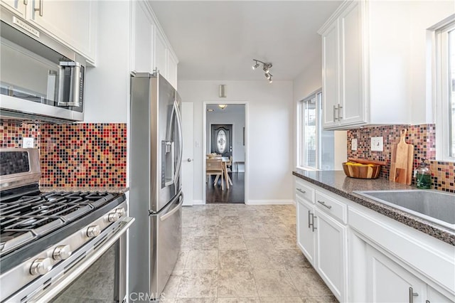 kitchen with dark stone countertops, backsplash, white cabinets, and appliances with stainless steel finishes