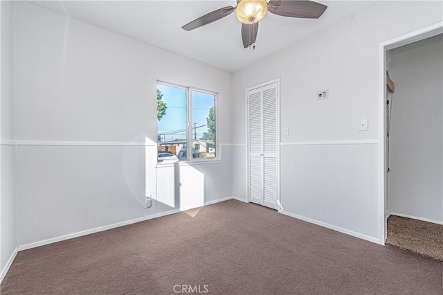 carpeted spare room with ceiling fan and a wainscoted wall