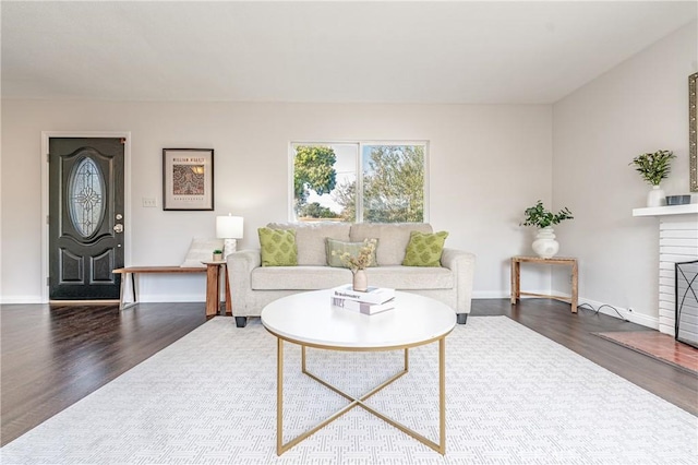 living area featuring a brick fireplace, baseboards, and wood finished floors