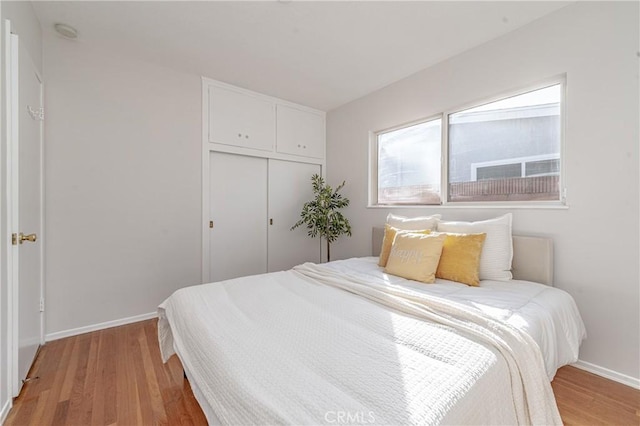 bedroom with light wood finished floors, a closet, and baseboards