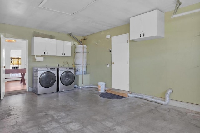 washroom with cabinets, strapped water heater, and washer and dryer