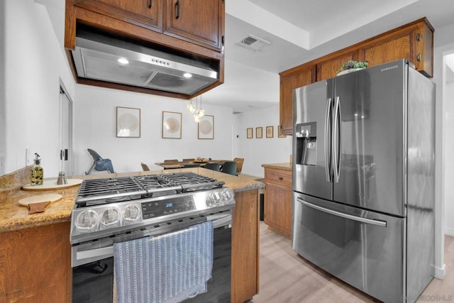 kitchen with wall chimney range hood, light wood-type flooring, stainless steel appliances, and light stone countertops