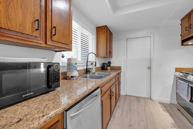 kitchen featuring light stone countertops, appliances with stainless steel finishes, sink, and light wood-type flooring