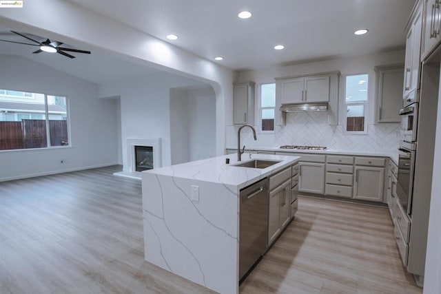 kitchen featuring appliances with stainless steel finishes, tasteful backsplash, lofted ceiling, sink, and a kitchen island with sink