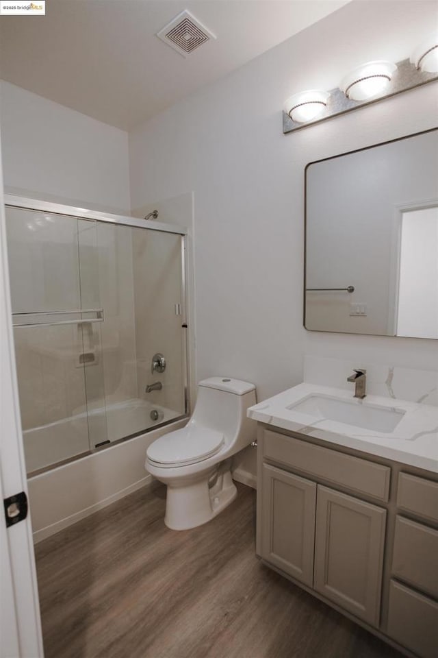 full bathroom with vanity, hardwood / wood-style flooring, combined bath / shower with glass door, and toilet