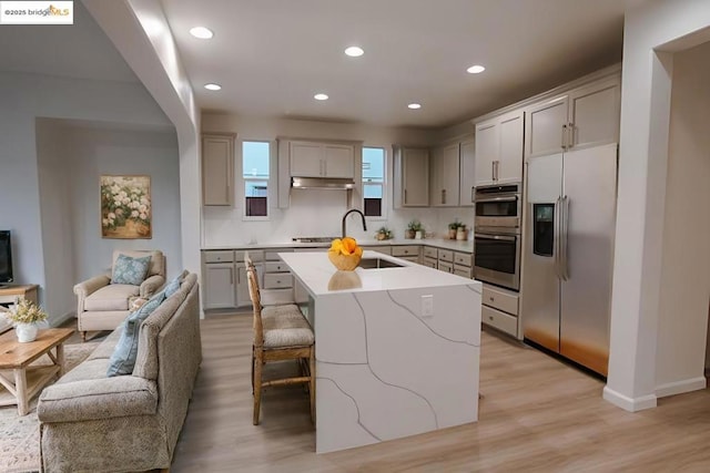 kitchen with sink, a breakfast bar area, a kitchen island with sink, stainless steel appliances, and light hardwood / wood-style floors