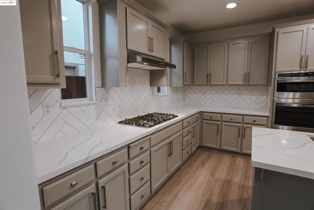 kitchen featuring tasteful backsplash, light hardwood / wood-style flooring, light stone countertops, and appliances with stainless steel finishes