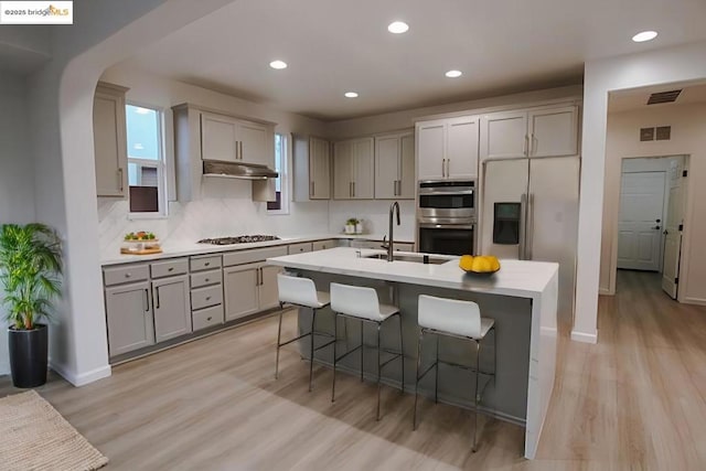 kitchen featuring sink, a breakfast bar, stainless steel appliances, light hardwood / wood-style floors, and an island with sink