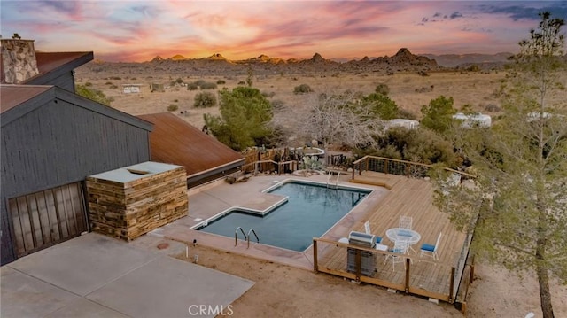 pool at dusk with grilling area, a deck with mountain view, and a patio area