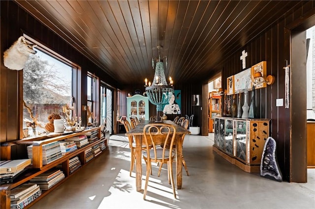 dining room with a notable chandelier, wooden walls, wooden ceiling, and concrete floors