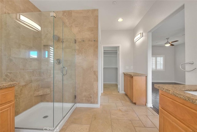 bathroom with a stall shower, stone tile floors, baseboards, a ceiling fan, and vanity