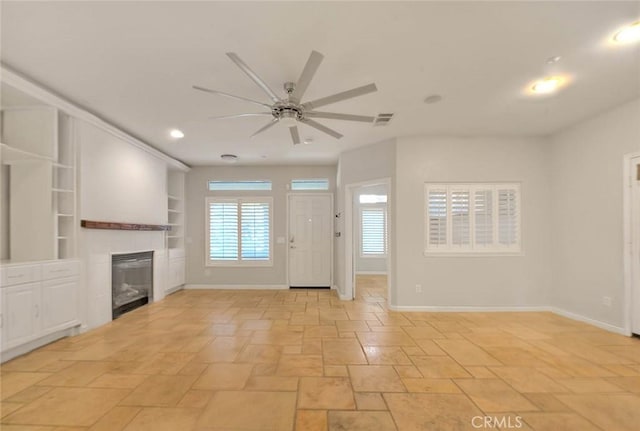 unfurnished living room with built in features, visible vents, a glass covered fireplace, ceiling fan, and baseboards