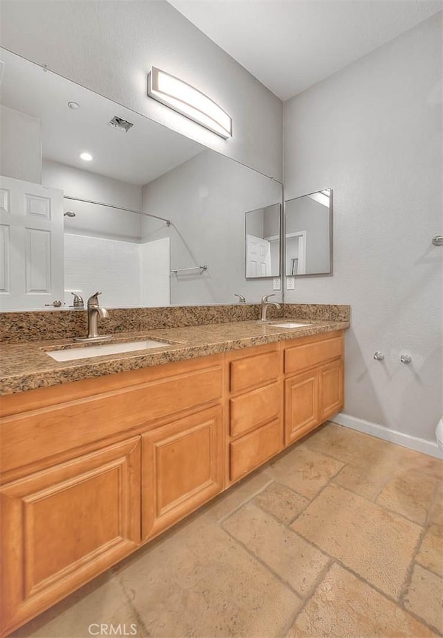 bathroom with double vanity, a sink, visible vents, and baseboards