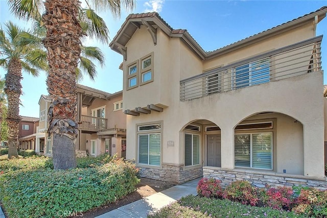 view of front of property with stone siding, a balcony, and stucco siding