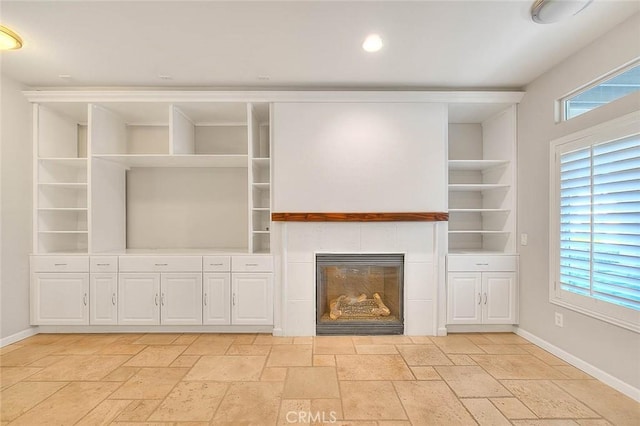 unfurnished living room featuring built in features, a tiled fireplace, baseboards, and stone tile floors