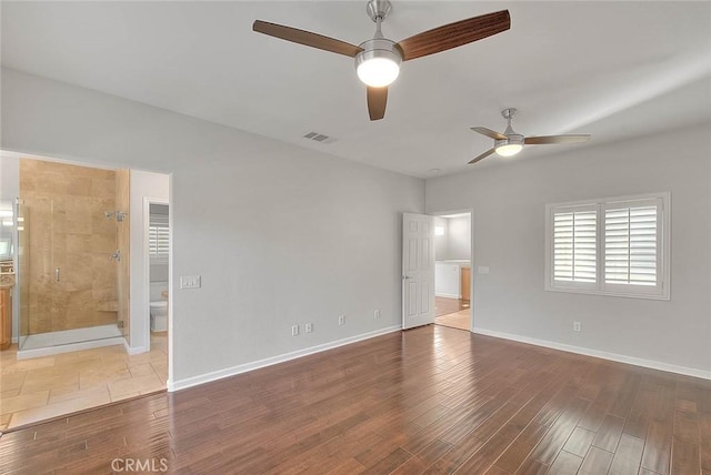 unfurnished bedroom featuring wood finished floors, a ceiling fan, visible vents, baseboards, and ensuite bath