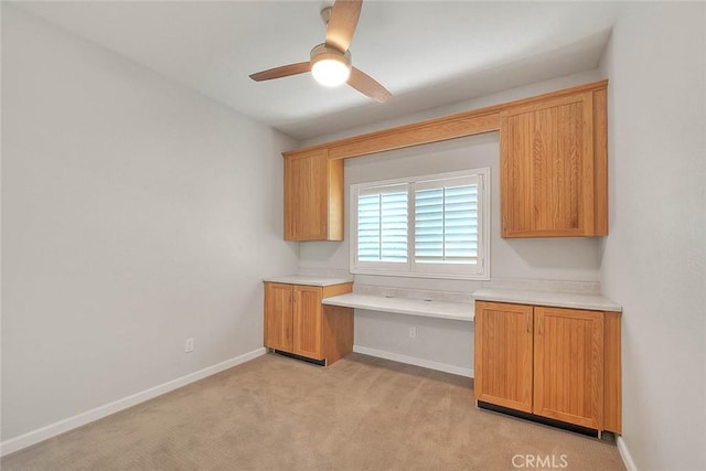 kitchen featuring light countertops, light carpet, built in desk, and baseboards