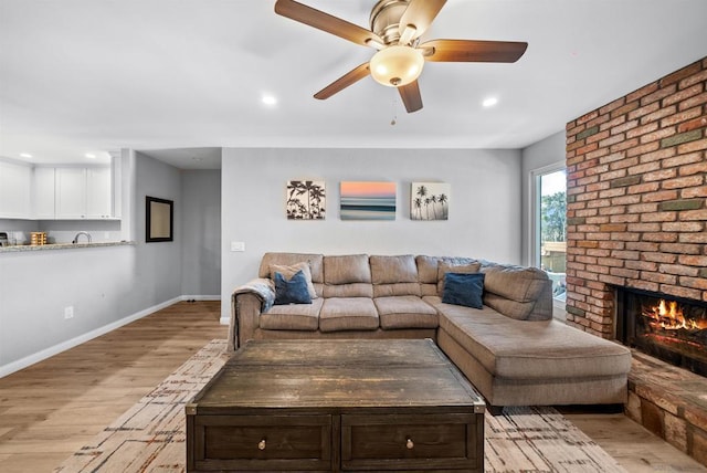 living room with sink, a fireplace, ceiling fan, and light wood-type flooring