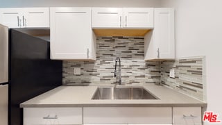 kitchen with tasteful backsplash, white cabinetry, black fridge, and sink