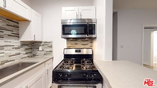 kitchen with appliances with stainless steel finishes, sink, white cabinets, and backsplash