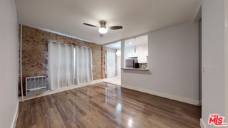 unfurnished living room with heating unit, dark wood-type flooring, and ceiling fan