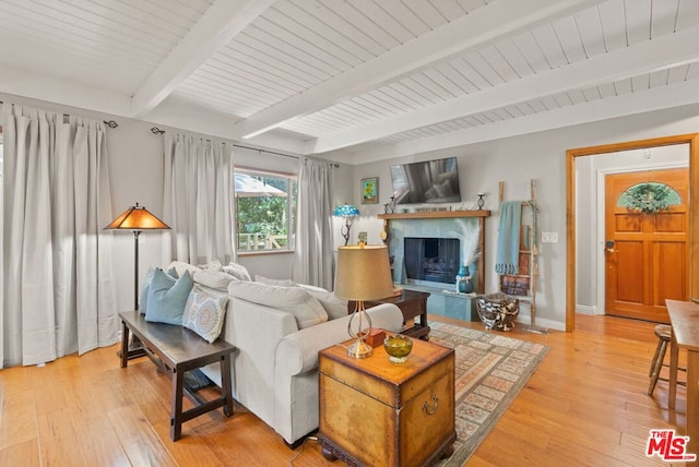 living room with beamed ceiling, a premium fireplace, and light wood-type flooring