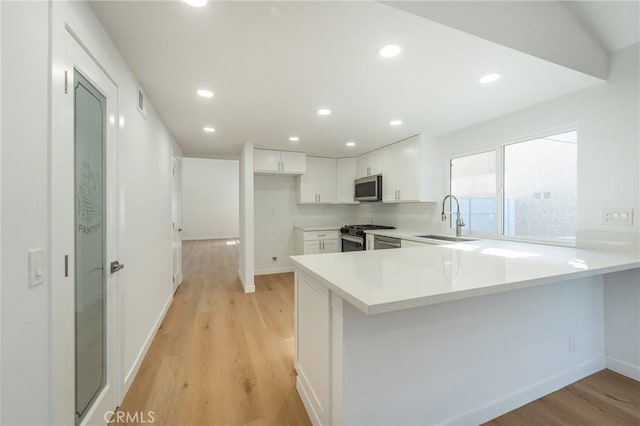 kitchen featuring sink, light hardwood / wood-style flooring, appliances with stainless steel finishes, white cabinets, and kitchen peninsula