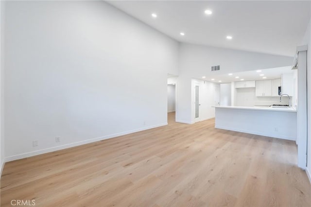 unfurnished living room with high vaulted ceiling, sink, and light wood-type flooring