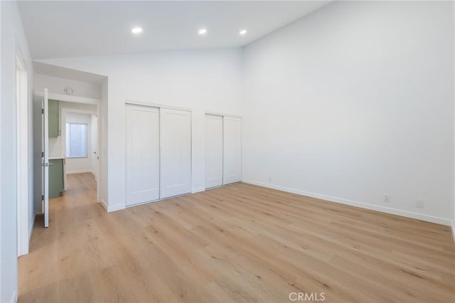 unfurnished bedroom with multiple closets, high vaulted ceiling, and light hardwood / wood-style floors